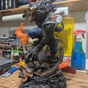 May include: A detailed figurine of a werewolf in a dynamic pose, with a snarling expression and claws extended. The figure is dark gray with blue pants and a torn white shirt, pierced by arrows. Orange flames and a broken frame add to the dramatic scene.