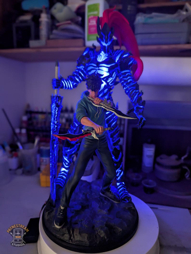 May include: A collectible figurine featuring a character in a blue hoodie and dark pants holding two daggers, standing in front of a glowing blue spectral warrior figure with a red ponytail and a large sword, all mounted on a dark rocky base.