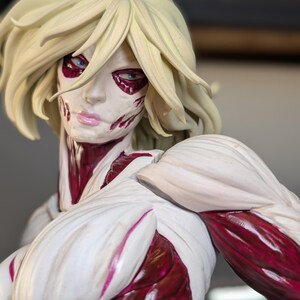 May include: A detailed figurine of a humanoid character with blonde hair, pale white skin, and exposed deep red muscle tissue. The figure features a stern facial expression with light blue eyes and pink lips, showcasing intricate anatomical textures.