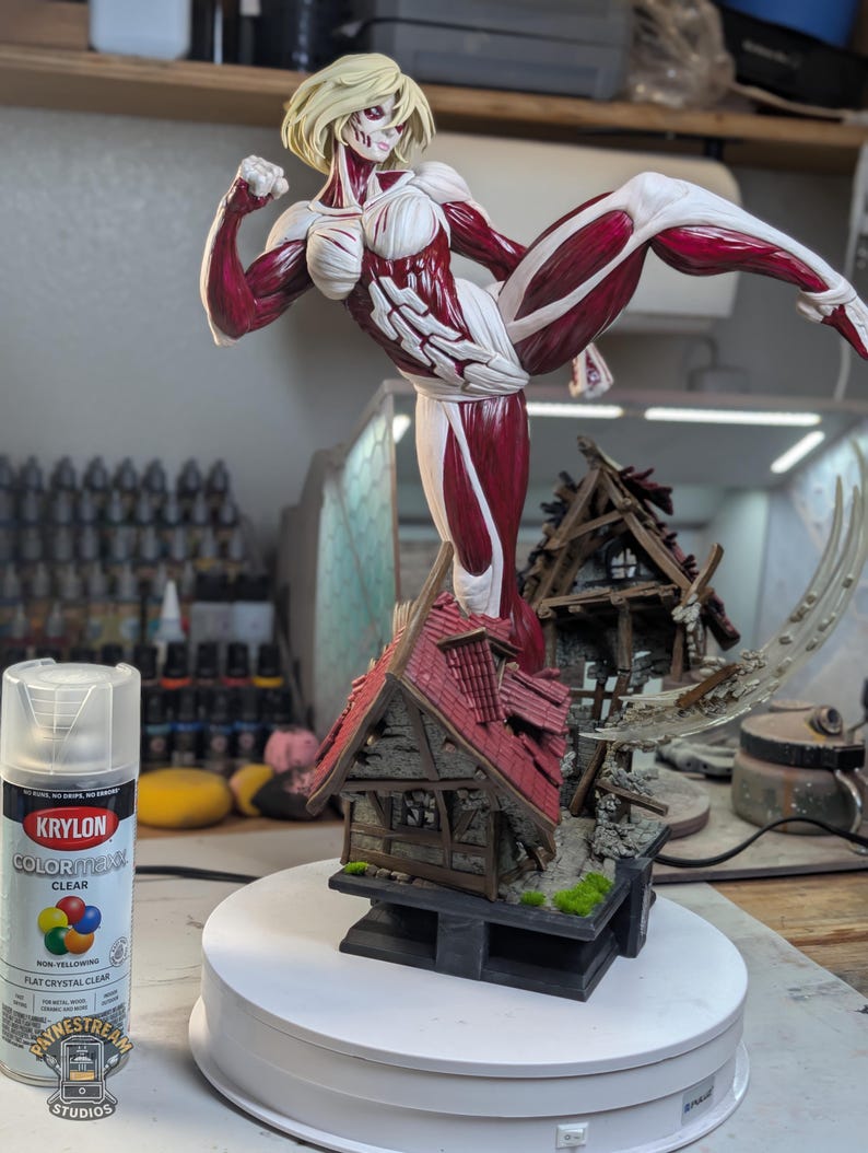 May include: A hand-painted figurine of a blonde female titan with exposed red muscle tissue and white bone-like armor, captured in a high-kick pose atop a ruined, shingled house structure. A can of Krylon ColorMaxx clear spray paint stands nearby.