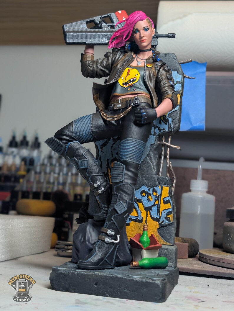 May include: A detailed collectible figurine of a character with bright pink hair, wearing a brown leather jacket, gray crop top with a yellow graphic, and black pants. The figure holds a black rifle and stands on a base with graffiti.