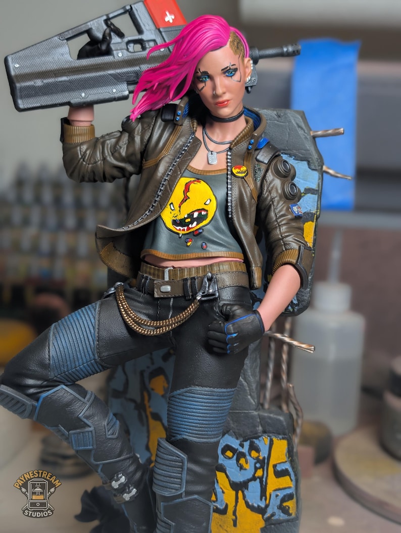 May include: A detailed action figure featuring a character with bright pink hair, wearing a brown leather jacket over a gray crop top with a yellow graphic print. The figure holds a black futuristic rifle and wears black pants with blue accents and a gold chain.