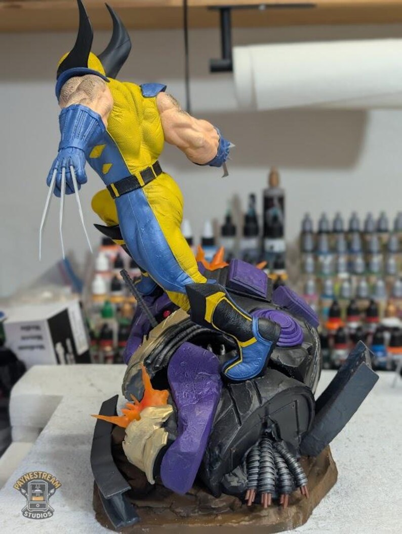 May include: A detailed figurine of Wolverine in a dynamic pose, wearing his classic yellow and blue costume. The figure has sharp claws extended and is positioned atop a detailed, multi-colored base. The figurine is a collectible item.