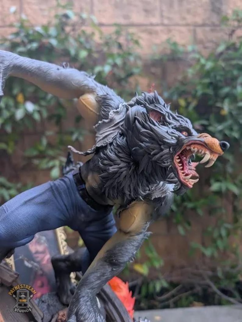 May include: A detailed figurine of a werewolf in a dynamic pose, with a snarling expression and exposed fangs. The figure has gray fur, red eyes, and is wearing blue jeans. The base of the figure has the text "PAYNESTREAM STUDIOS".