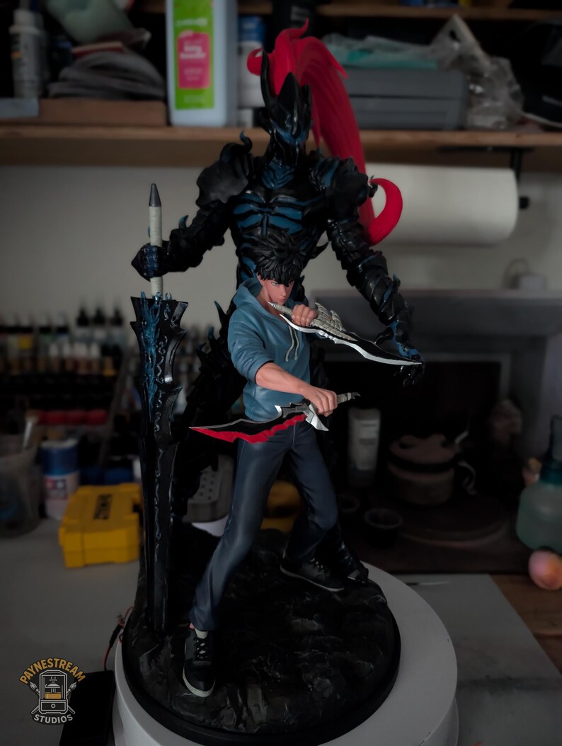May include: A detailed figurine featuring a character in a blue hoodie and dark pants holding two daggers, standing in front of a tall, dark, armored shadow figure with a red ponytail and a large black sword with blue glowing accents.