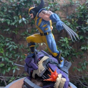 May include: A Wolverine action figure in a dynamic pose, clad in a yellow and blue costume with black accents. The figure has extended claws and is standing on a purple and gray robotic structure. The base has the text "Paynestream Studios".