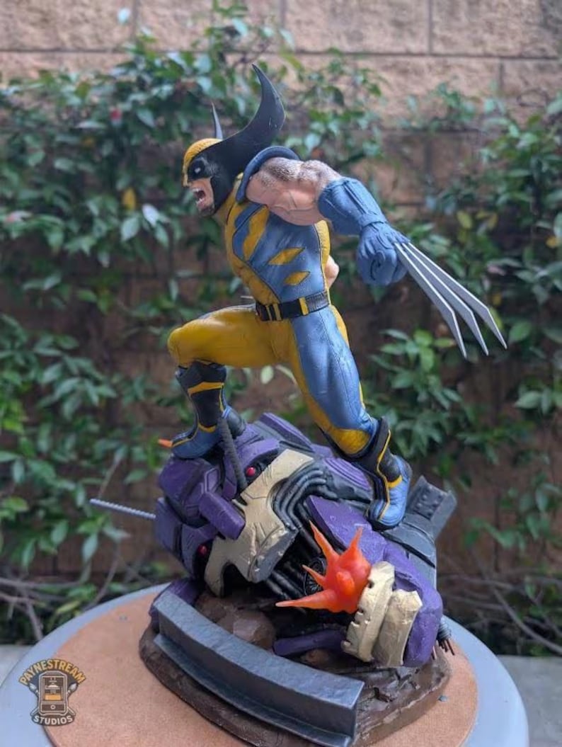 May include: A Wolverine action figure in a dynamic pose, clad in a yellow and blue costume with black accents. The figure has extended claws and is standing on a purple and gray robotic structure. The base has the text "Paynestream Studios".