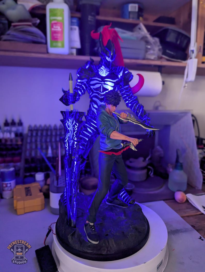 May include: A detailed figurine featuring a young person in a green hoodie and dark pants standing in front of a large, dark, skeletal shadow figure with glowing blue accents and a red ponytail, holding a large sword and two smaller daggers.