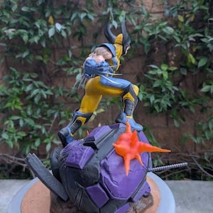May include: A Wolverine action figure in a dynamic pose, clad in a yellow and blue costume. The figure stands atop a purple and gray base with an orange starburst element. The figure has black claws and a detailed facial expression.