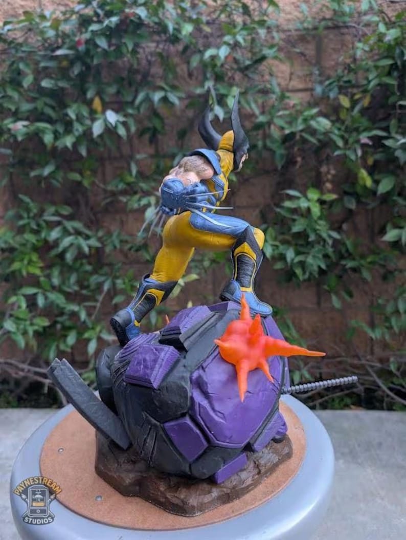 May include: A Wolverine action figure in a dynamic pose, clad in a yellow and blue costume. The figure stands atop a purple and gray base with an orange starburst element. The figure has black claws and a detailed facial expression.