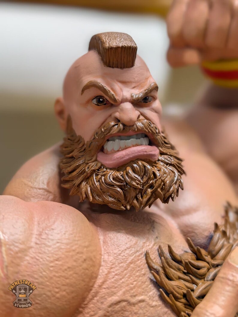 Puede incluir: Una figura detallada de un personaje musculoso con peinado mohawk, una barba marr&oacute;n espesa y una expresi&oacute;n facial agresiva que muestra los dientes. La figura tiene piel bronceada, hombros anchos y una prenda texturizada de color marr&oacute;n.