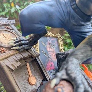 May include: A detailed statue featuring a clock tower with a pendulum, a framed portrait, and a figure with clawed hands and blue clothing. The clock shows the time as 10:09. The statue has a weathered, aged appearance.