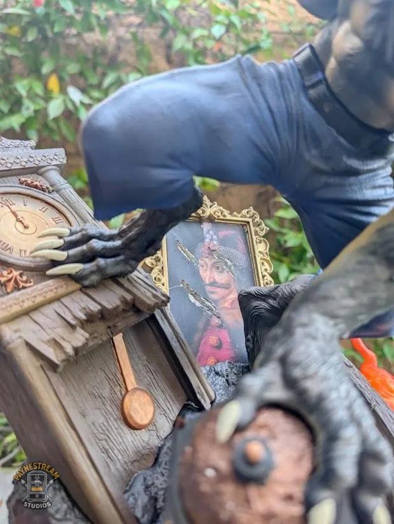 May include: A detailed statue featuring a clock tower with a pendulum, a framed portrait, and a figure with clawed hands and blue clothing. The clock shows the time as 10:09. The statue has a weathered, aged appearance.