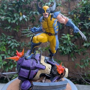 May include: A detailed figurine of Wolverine in a dynamic pose, clad in a yellow and blue costume, with claws extended. He stands atop a damaged purple and gold robotic figure, with fiery orange accents. The base has the "Paynestream Studios" logo.