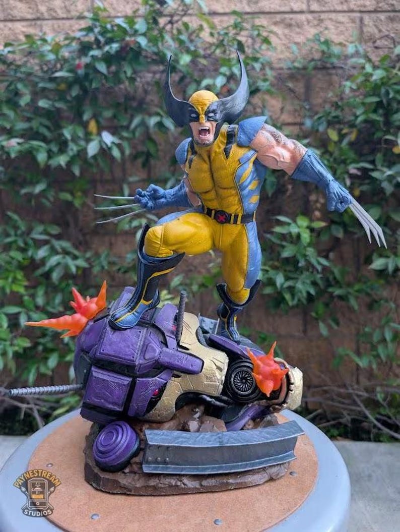 May include: A detailed figurine of Wolverine in a dynamic pose, clad in a yellow and blue costume, with claws extended. He stands atop a damaged purple and gold robotic figure, with fiery orange accents. The base has the "Paynestream Studios" logo.