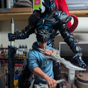 May include: A detailed figurine featuring a dark armored warrior with a long red ponytail standing behind a person in a blue hoodie. The warrior holds a tall sword, while the person in the hoodie wields two curved blades. A logo reads Paynestream Studios.