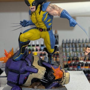 May include: A Wolverine figurine in a dynamic pose, clad in a yellow and blue costume, with claws extended. The figure stands atop a purple and gold robotic head, with fiery orange bursts. The base features the "Paynestream Studios" logo.
