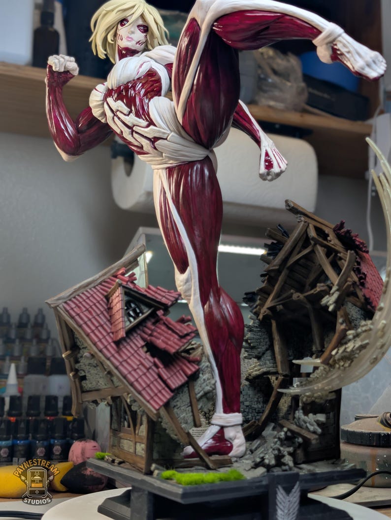 May include: A detailed figurine of a blonde character with exposed red muscle tissue and white skin, captured in a dynamic high-kick pose. The figure stands atop a base featuring a miniature, partially destroyed house with a red tiled roof.