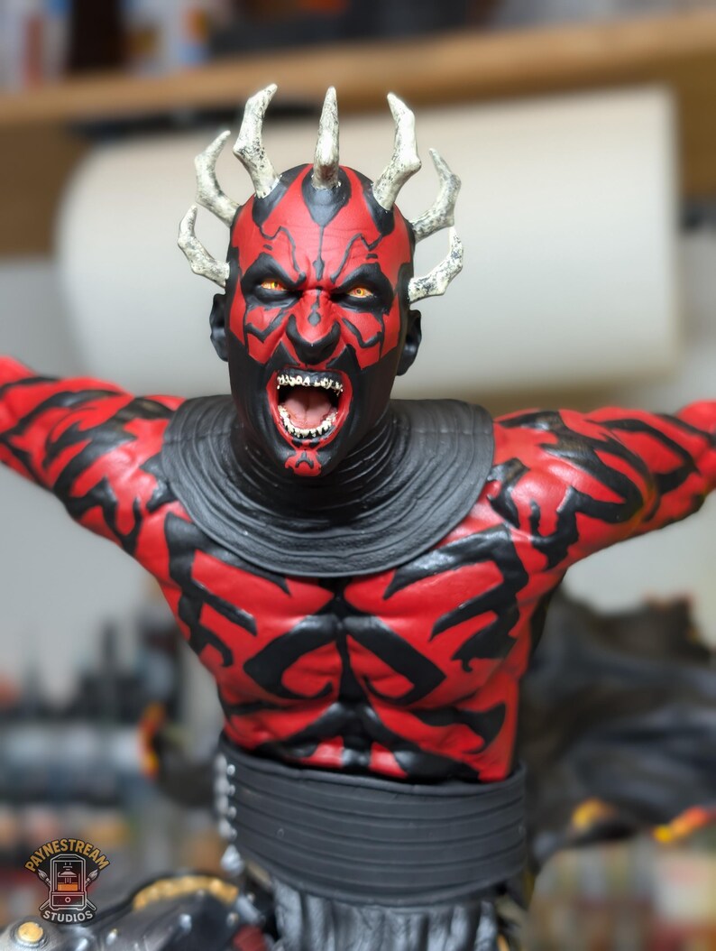 K&ouml;nnte beinhalten: Eine detaillierte Figur mit rot-schwarzem Hautmuster, gelben Augen und spitzen Z&auml;hnen, die eine Krone aus spitzen H&ouml;rnern auf dem Kopf tr&auml;gt. Die Figur tr&auml;gt einen dunklen Kragen und einen schwarzen G&uuml;rtel und zeigt eine dynamische Pose.