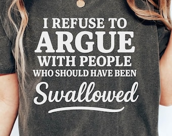 Könnte beinhalten: Dunkelgraues T-Shirt mit dem weißen Text "I REFUSE TO ARGUE WITH PEOPLE WHO SHOULD HAVE BEEN Swallowed". Das Shirt hat einen Rundhalsausschnitt und kurze Ärmel. Das Model trägt eine blaue Jeans.