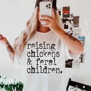 Puede incluir: Camiseta blanca con texto negro que dice "criando pollos y ni&ntilde;os salvajes."