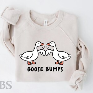 May include: A beige sweatshirt with a graphic of two geese bumping their wings together. The text "Goose Bumps" is printed below the geese.