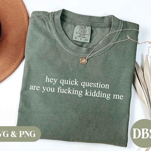 Puede incluir: Una camiseta de manga corta color verde oliva con cuello redondo y el texto en blanco "hey quick question are you fucking kidding me" impreso en el frente. La prenda incluye una etiqueta de la marca Comfort Colors y un pequeño collar.