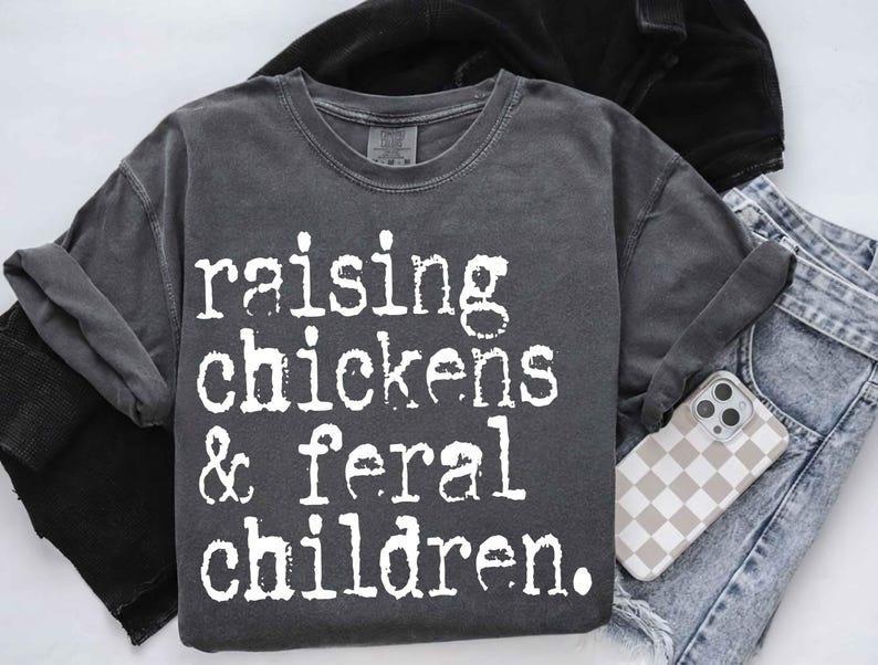 Puede incluir: Una camiseta gris oscura con el texto "raising chickens & feral children." impreso en blanco.