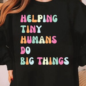 May include: Black sweatshirt with the text "Helping Tiny Humans Do Big Things" in rainbow colors.