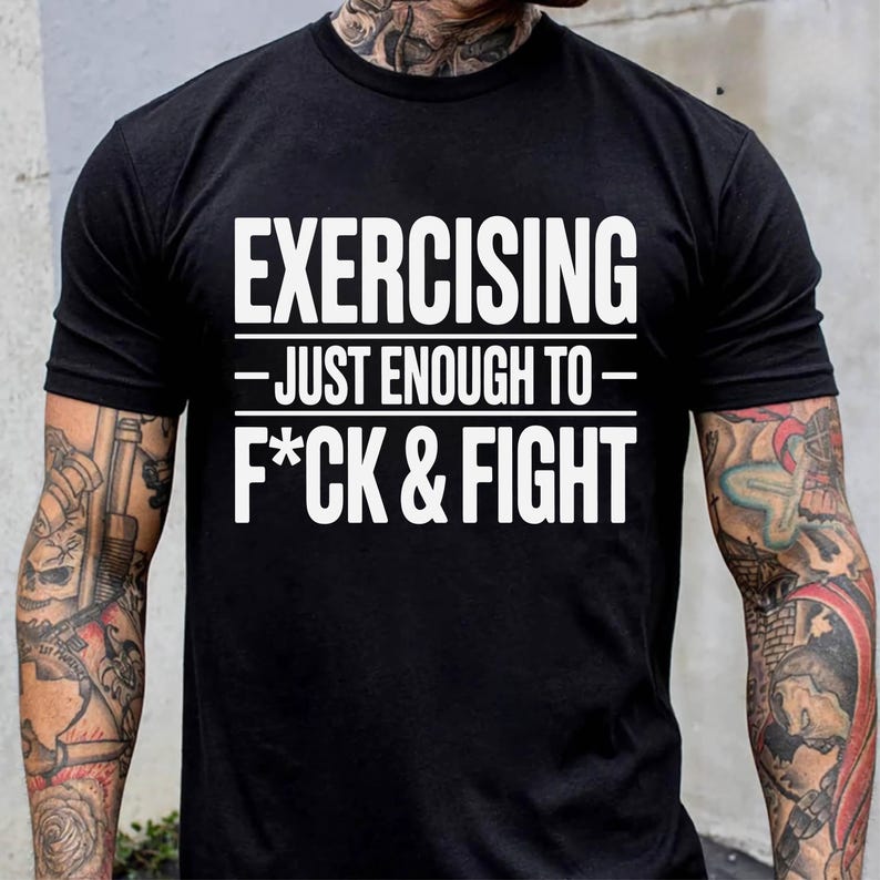 May include: Black t-shirt with the white text "EXERCISING - JUST ENOUGH TO - F*CK & FIGHT". The shirt has short sleeves and a crew neck. The person wearing the shirt has tattoos on their arms and neck.