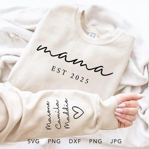 Op de afbeelding: Een wit sweatshirt met de tekst "mama est 2025" op de voorkant en de namen "Masone, Camilla, Maddie" op de mouw.