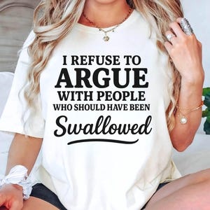 K&ouml;nnte beinhalten: Cremefarbenes T-Shirt mit dem schwarzen Text "I REFUSE TO ARGUE WITH PEOPLE WHO SHOULD HAVE BEEN SWALLOWED". Das Shirt ist ein l&auml;ssiger Stil mit kurzen &Auml;rmeln.