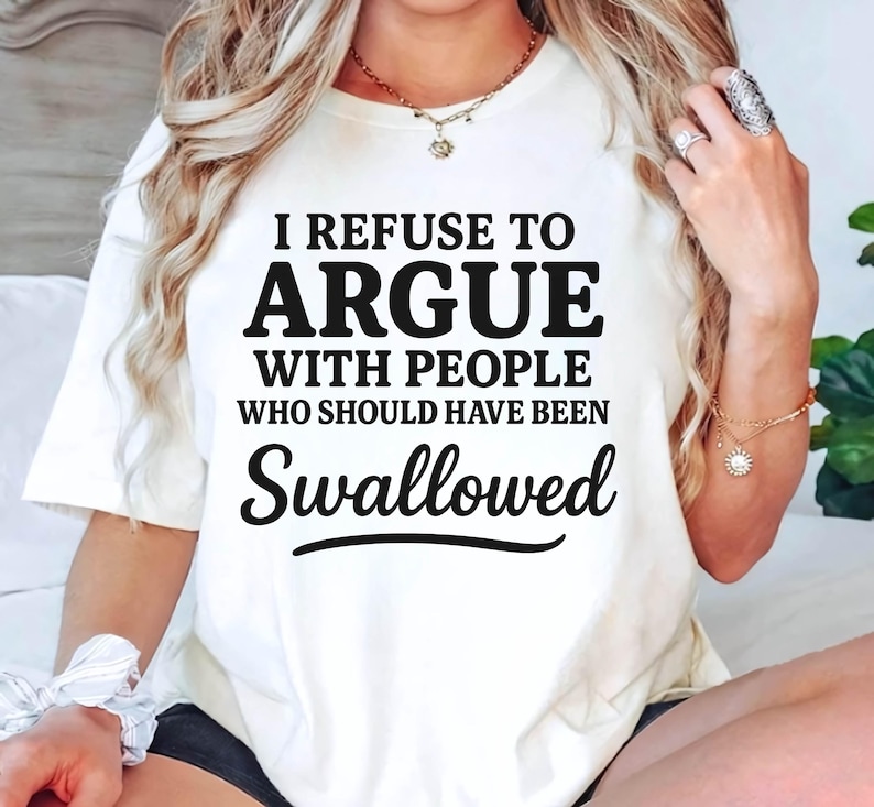 K&ouml;nnte beinhalten: Cremefarbenes T-Shirt mit dem schwarzen Text "I REFUSE TO ARGUE WITH PEOPLE WHO SHOULD HAVE BEEN SWALLOWED". Das Shirt ist ein l&auml;ssiger Stil mit kurzen &Auml;rmeln.