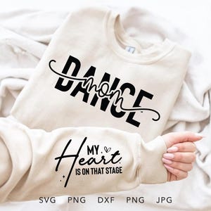 May include: A cream-colored sweatshirt with the words "DANCE mom" in black script. The sleeve displays the text "My heart is on that stage" with a heart symbol. The bottom of the image shows file type options: SVG, PNG, DXF, PNG, JPG.
