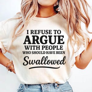 K&ouml;nnte beinhalten: Cremefarbenes Sweatshirt mit dem schwarzen Text: "I REFUSE TO ARGUE WITH PEOPLE WHO SHOULD HAVE BEEN SWALLOWED". Das Shirt hat einen Rundhalsausschnitt und lange &Auml;rmel.