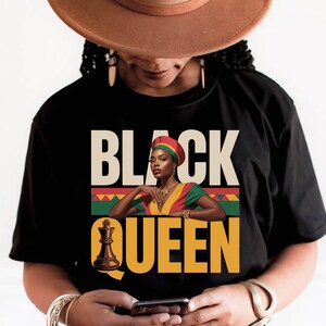 May include: A black t-shirt featuring a graphic print of a person wearing a red, yellow, and green headwrap and matching top. The text reads BLACK QUEEN, with the letter Q replaced by a brown chess king piece, set against a geometric pattern.