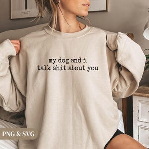 May include: A beige sweatshirt with the text "my dog and i talk shit about you" in black. The sweatshirt has a crew neck and long sleeves. The image also includes the text "PNG & SVG".