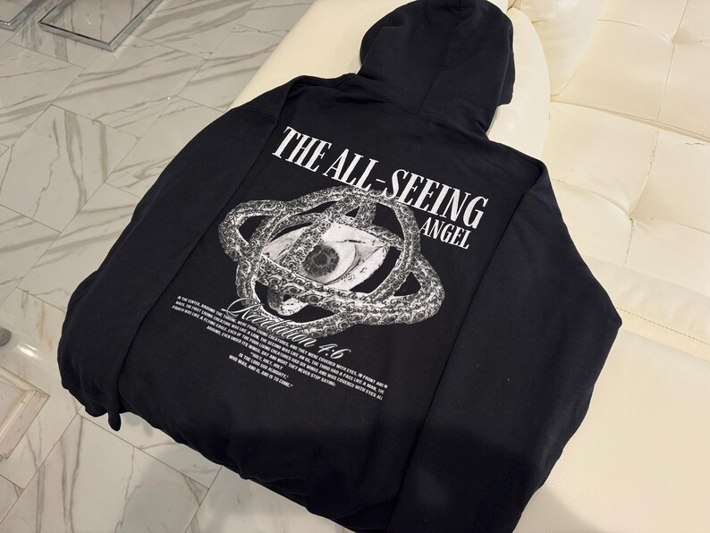 May include: Black hooded sweatshirt with the text "THE ALL-SEEING ANGEL" and an eye graphic. The graphic is surrounded by a serpent-like design. The text "Revelation 4:6" is also visible.