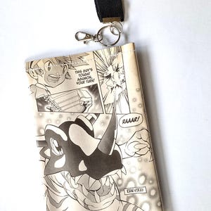 May include: A black and white manga-style wallet with a black lanyard and silver-colored clasp. The wallet features panels from a comic book with characters and speech bubbles. The text on the wallet reads "THIS GUY'S TOUGH! AGUMON, YOUR TURN!" and "RAAAR!"