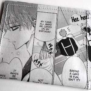 May include: A rectangular wallet featuring a black and white manga print with panels showing characters baking. Text bubbles read: My fans all make me cakes on my birthday, It makes me happy, Baking a cake is fun, isn't it?, Hee hee!, and Wsk.