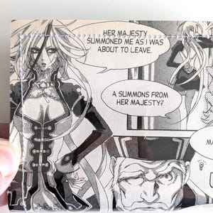 May include: A handmade wallet featuring a manga panel with black and white illustrations. The panel includes speech bubbles with text, and a detailed drawing of a female character. The wallet is stitched with white thread.