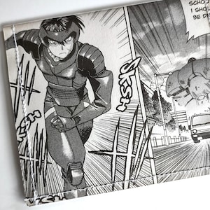 May include: Black and white manga-style wallet featuring a dynamic action scene with a character in armor. The wallet has a rectangular shape with a stitched border and includes text from the manga.