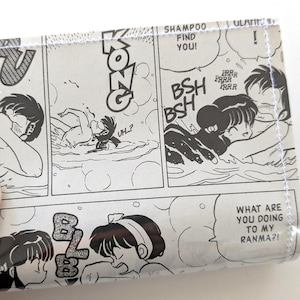 May include: A wallet featuring panels from a black and white manga comic. The comic strip shows characters in a swimming scene with speech bubbles and sound effects. The text includes "KONG", "SHAMPOO FIND YOU!", and "WHAT ARE YOU DOING TO MY RANMA?!"