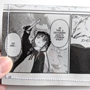 May include: A wallet featuring panels from a manga comic. The panels depict a character holding a weapon, with speech bubbles that read "No way..." and "Is this a legendary hero's cypress stick?" The final panel shows a wolf and the word "DEAD..."