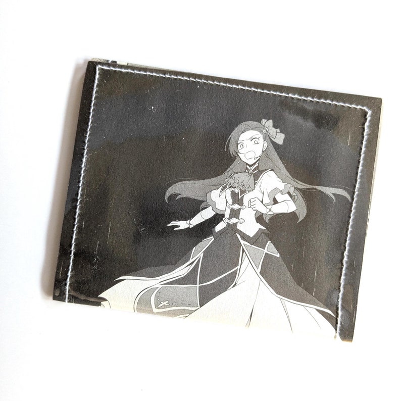 Puede incluir: Una ilustraci&oacute;n en blanco y negro de una ni&ntilde;a con el pelo largo que lleva un vestido y sostiene una espada. La ilustraci&oacute;n est&aacute; impresa en una cartera de tela negra.