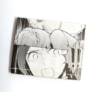 Puede incluir: Una ilustraci&oacute;n en blanco y negro de estilo manga de una mujer con los ojos muy abiertos y la boca abierta, que parece sorprendida o asustada. La imagen est&aacute; impresa en una cartera de tela.