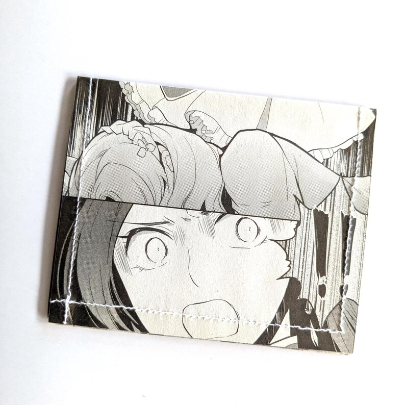 Puede incluir: Una ilustraci&oacute;n en blanco y negro de estilo manga de una mujer con los ojos muy abiertos y la boca abierta, que parece sorprendida o asustada. La imagen est&aacute; impresa en una cartera de tela.