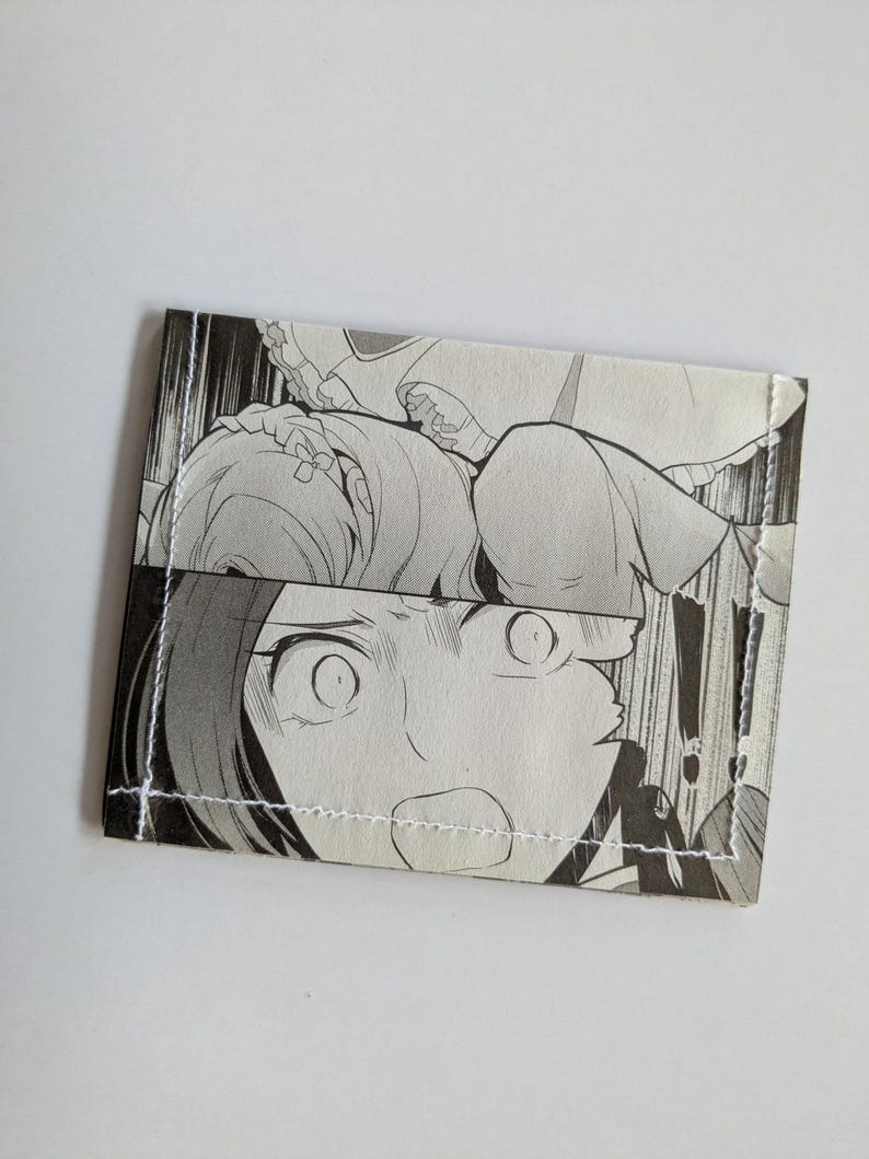 Puede incluir: Una cartera en blanco y negro hecha de un c&oacute;mic manga. La cartera presenta un primer plano de la cara de un personaje con ojos grandes y la boca abierta.
