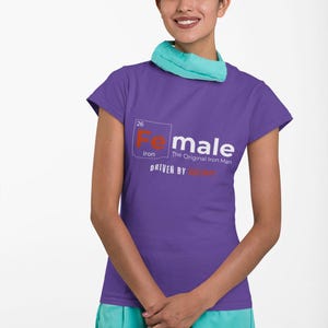 Puede incluir: Camiseta morada de manga corta con un gr&aacute;fico blanco de un elemento de la tabla peri&oacute;dica, "Fe" para el hierro, con el texto "Female, The Original Iron Man, Driven by Strength".