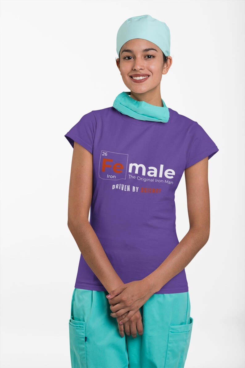 Puede incluir: Camiseta morada de manga corta con un gr&aacute;fico blanco de un elemento de la tabla peri&oacute;dica, "Fe" para el hierro, con el texto "Female, The Original Iron Man, Driven by Strength".